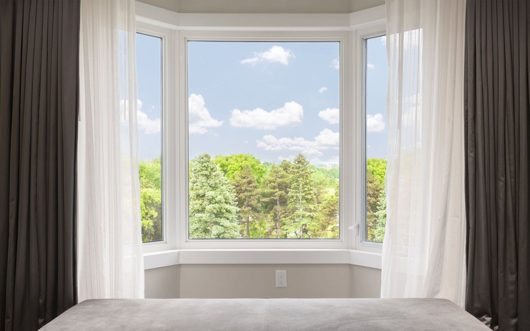 A bay window with clear glass looking out over green treetops