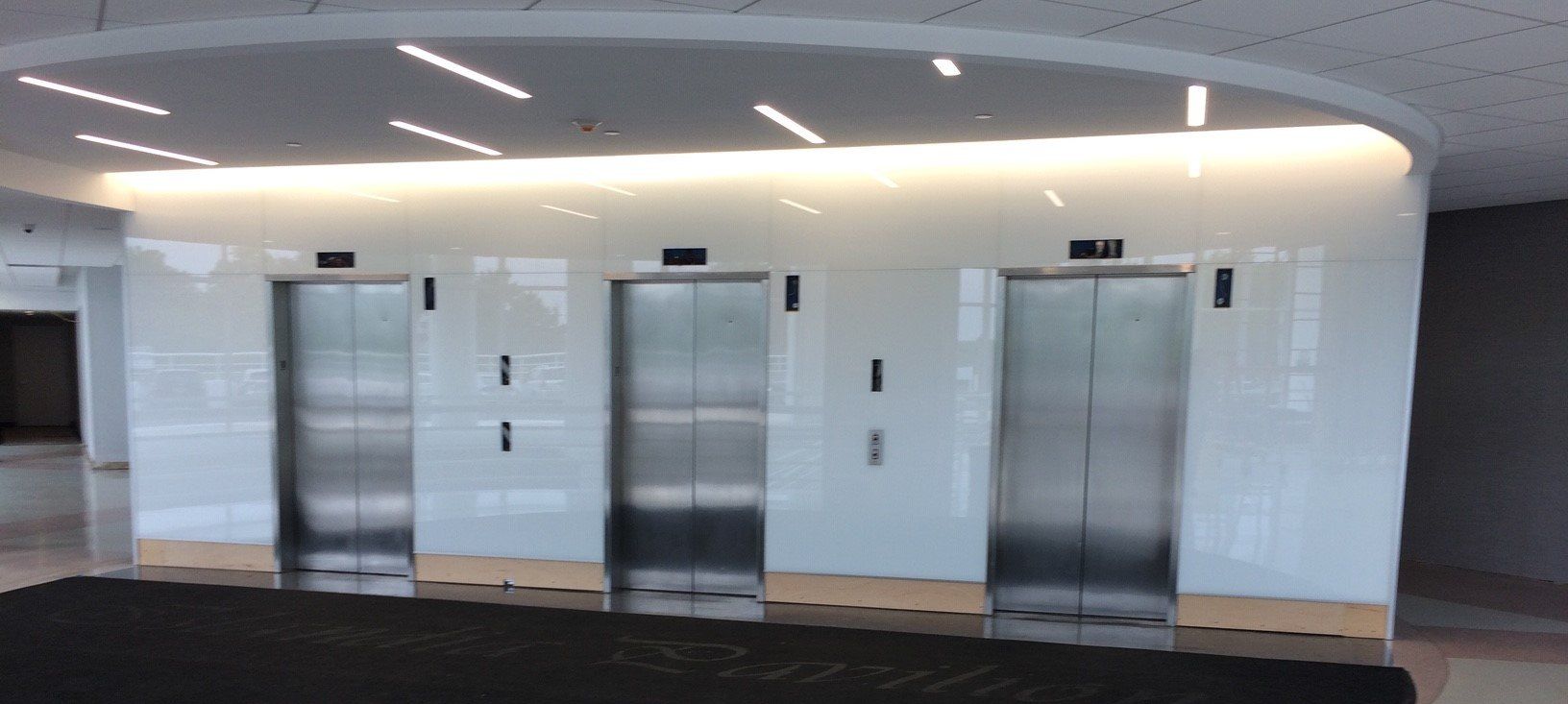 Back-painted glass wall panels installed around elevator doors in a commercial lobby