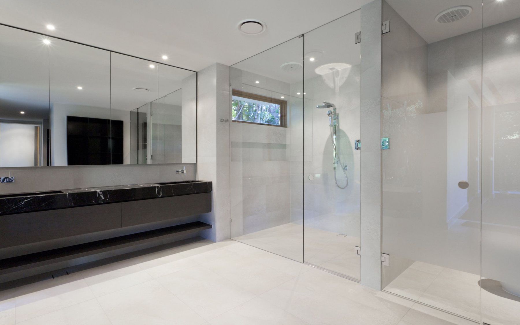 A walk-in frameless glass shower enclosure in a modern grey-tiled bathroom