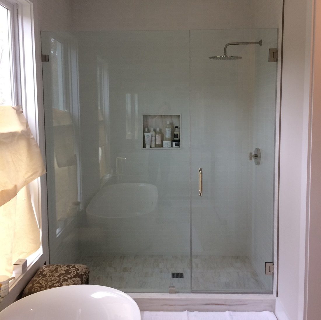 Frameless glass shower enclosure with a swing door in a tiled bathroom